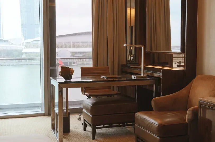 A compact yet efficient workspace is tucked next to a balcony door, featuring a glass desk, a leather office chair, and an adjacent reading armchair. Grouping functional furniture near natural light demonstrates how smart placement elevates smaller footprints.