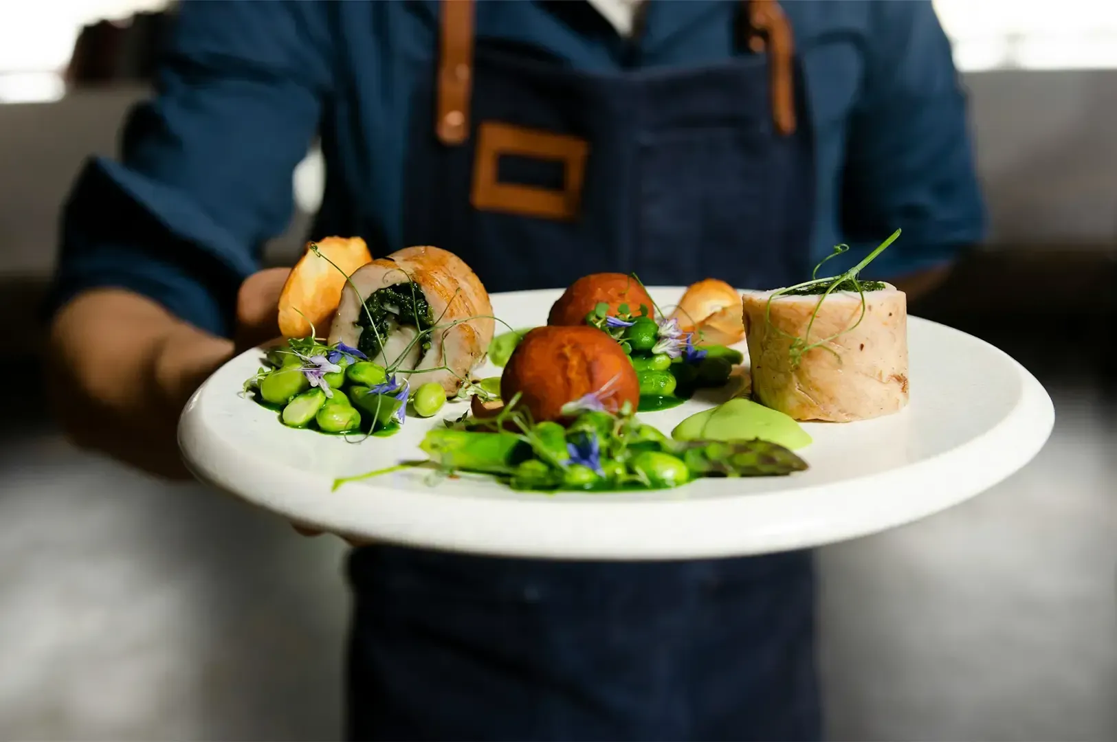 A waiter in dark blue outfit holding out a fine dining dish that on a white plate.