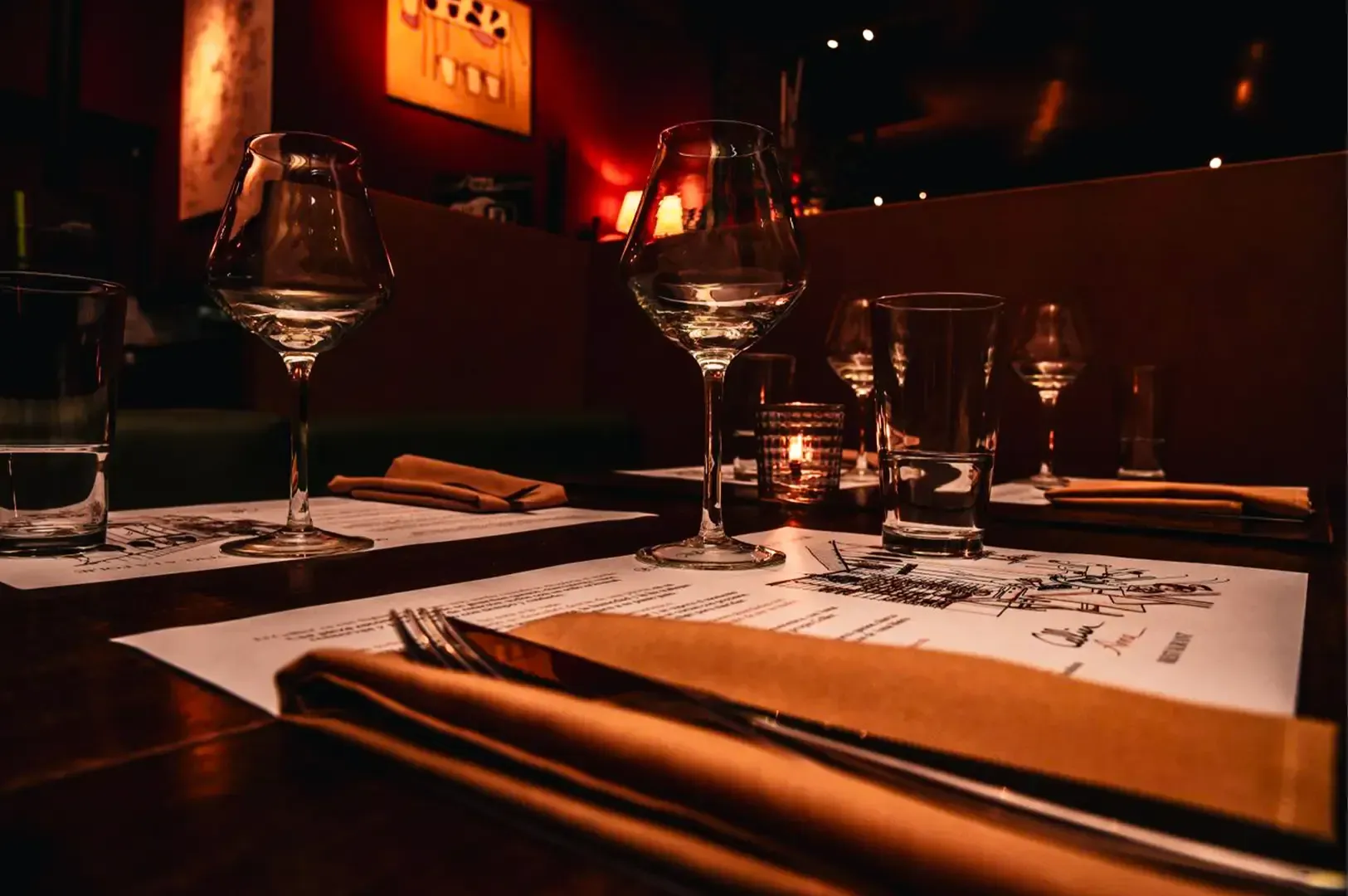 Angled close up shot of a fine dining dinner table with neatly arranged utensils and glasses with the dim interior slightly visible in the background.