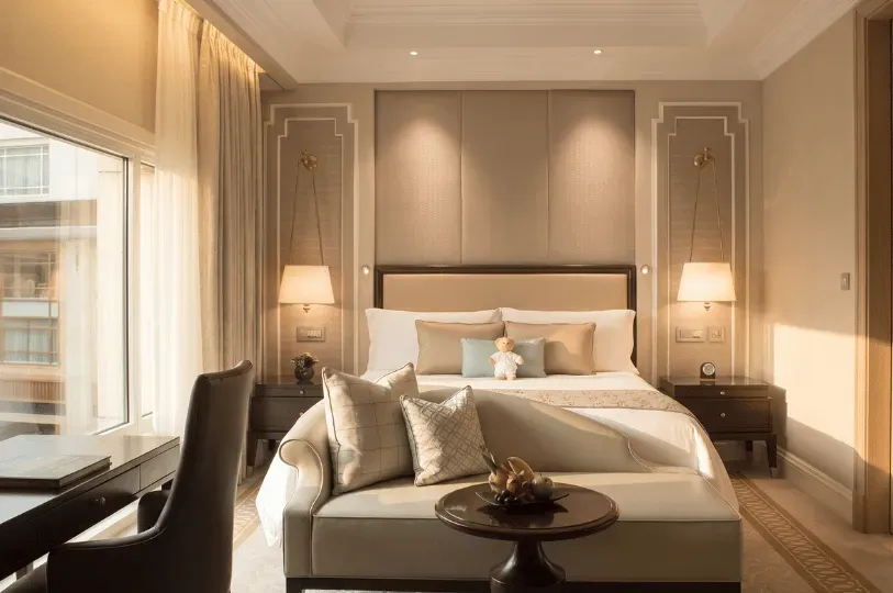 A front-facing view of a hotel bedroom shows a curved sofa and a small fruit table placed directly at the foot of the bed. Nesting these seating elements together creates a cozy, self-contained lounge area while preserving the room's central walkway.