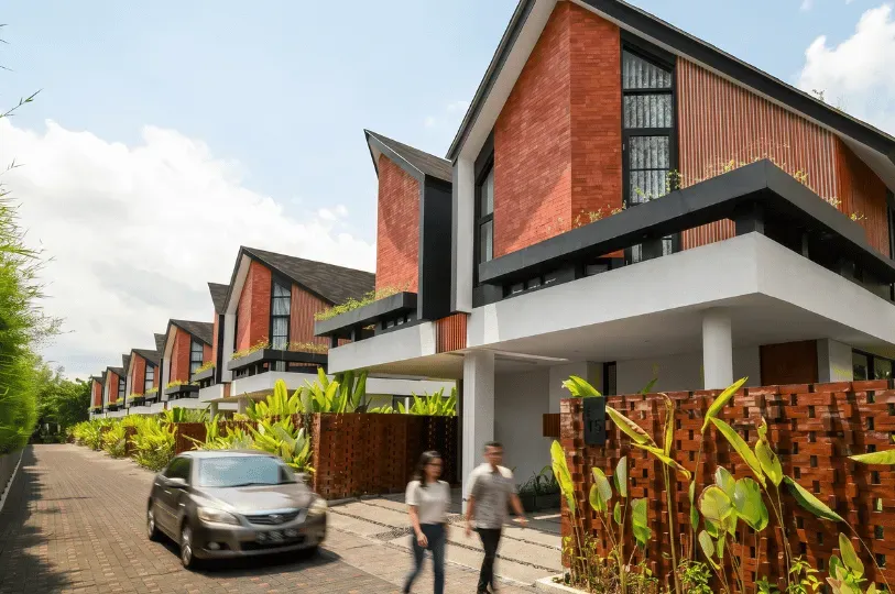 A row of modern luxury villas featuring striking pitched roofs and red brick facades lining a paved driveway in a Balinese development.