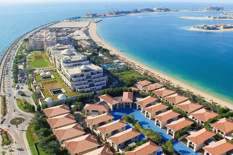 An expansive, highly manicured luxury resort and residential complex featuring uniform red-tiled roofs and sprawling, meandering blue pools built directly onto a manufactured coastline.