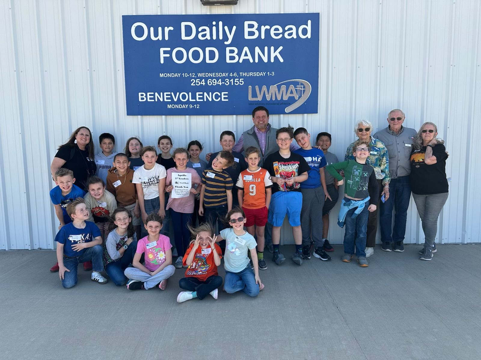 A large group of children and adults pose in front of a blue sign for the