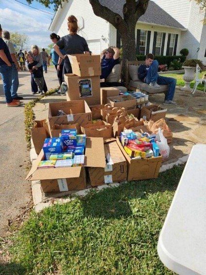 Boxes and bags of goods on a lawn, people nearby; possibly a yard sale or donation event.