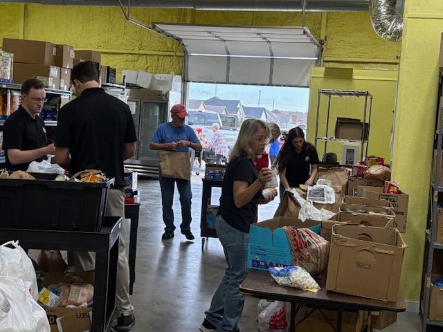Volunteers organize boxes of food and supplies inside a yellow-walled warehouse facility.