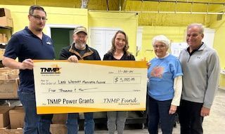 Five people stand in a room holding a large check for $5,000 from TNMP Power Grants to Lake Whitney Ministerial Alliance.