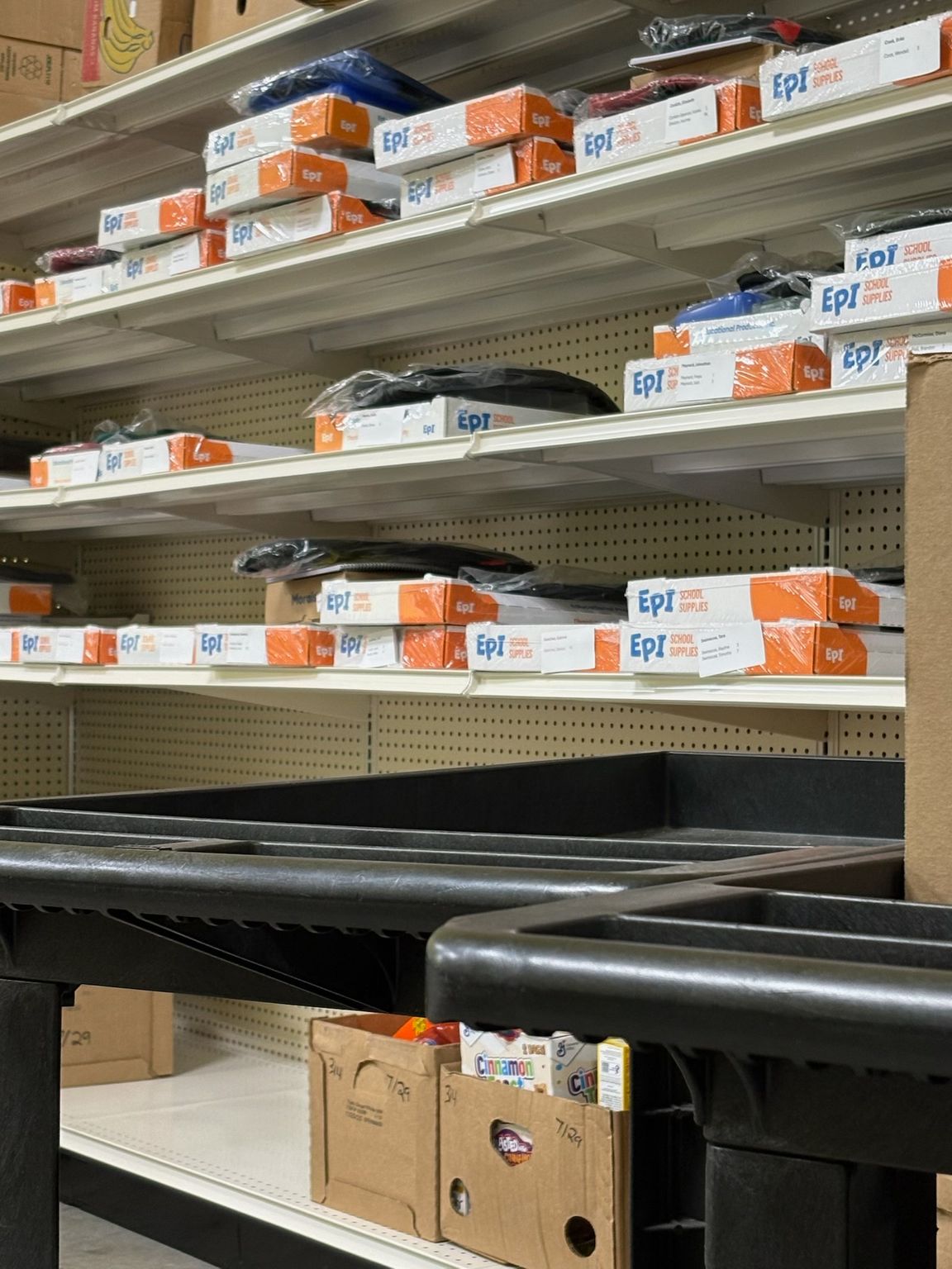Store shelves lined with orange-and-white boxes and black trays in an industrial aisle