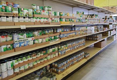 A supermarket aisle with long shelves stocked with numerous cans, organized in rows and grouped by cardboard trays.