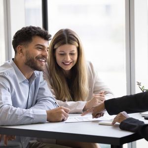 Happy couple engaged in conversation with advisor, realtor, or financial consultant, review agreement details, ready to sign contract, get professional services, feel satisfied with bank loan approval