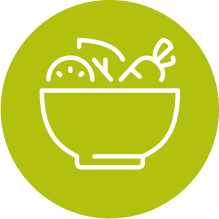 White bowl of vegetables, including a lemon slice and carrot, on a green background.