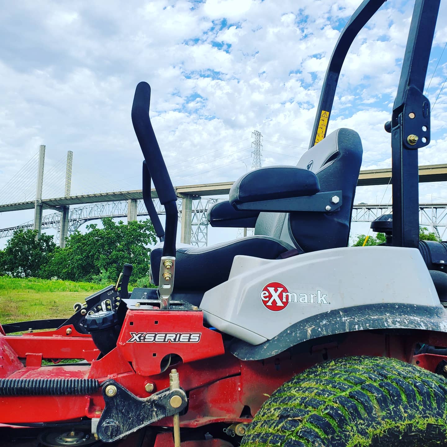 A red and white lawn mower with a bridge in the background