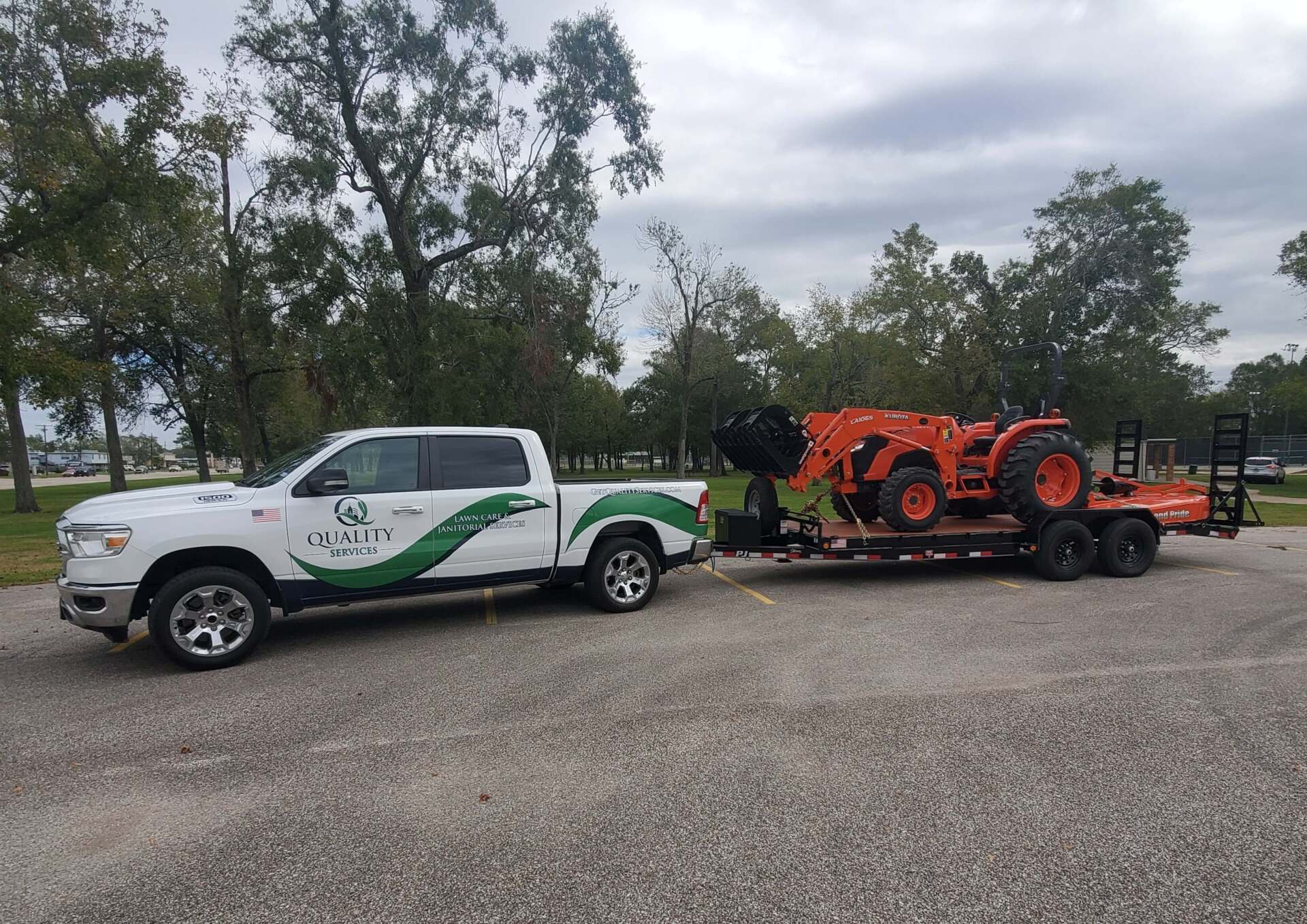A white truck is towing a red tractor on a trailer.