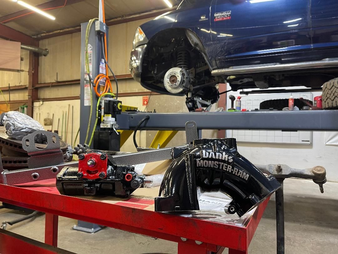 A car raised on a hydraulic lift in a garage with new black suspension and steering parts sitting on a red workbench. | Glen Cove Repair