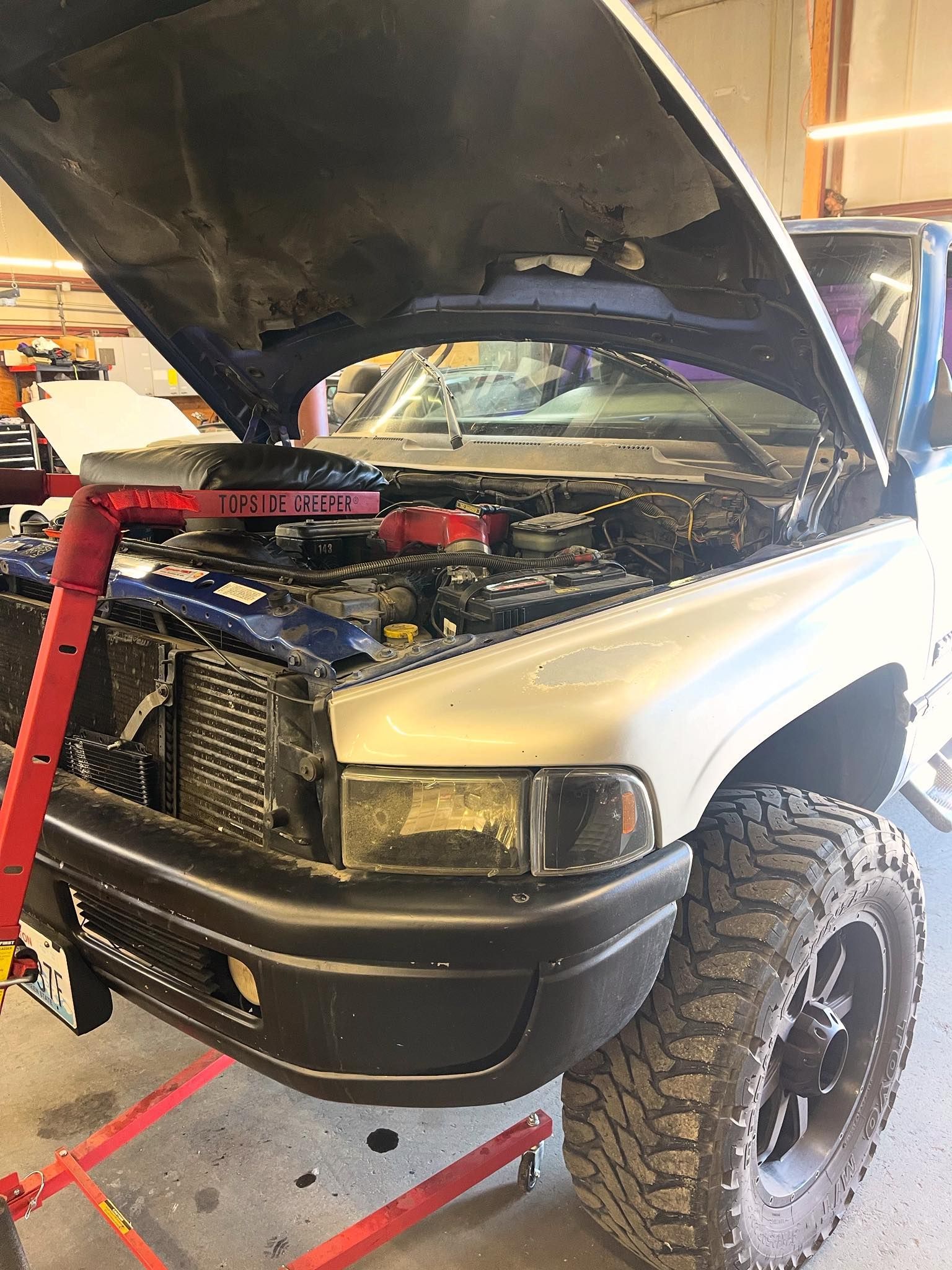 A white pickup truck with its hood open and a red engine hoist positioned over the front of the vehicle in a garage. | Glen Cove Repair