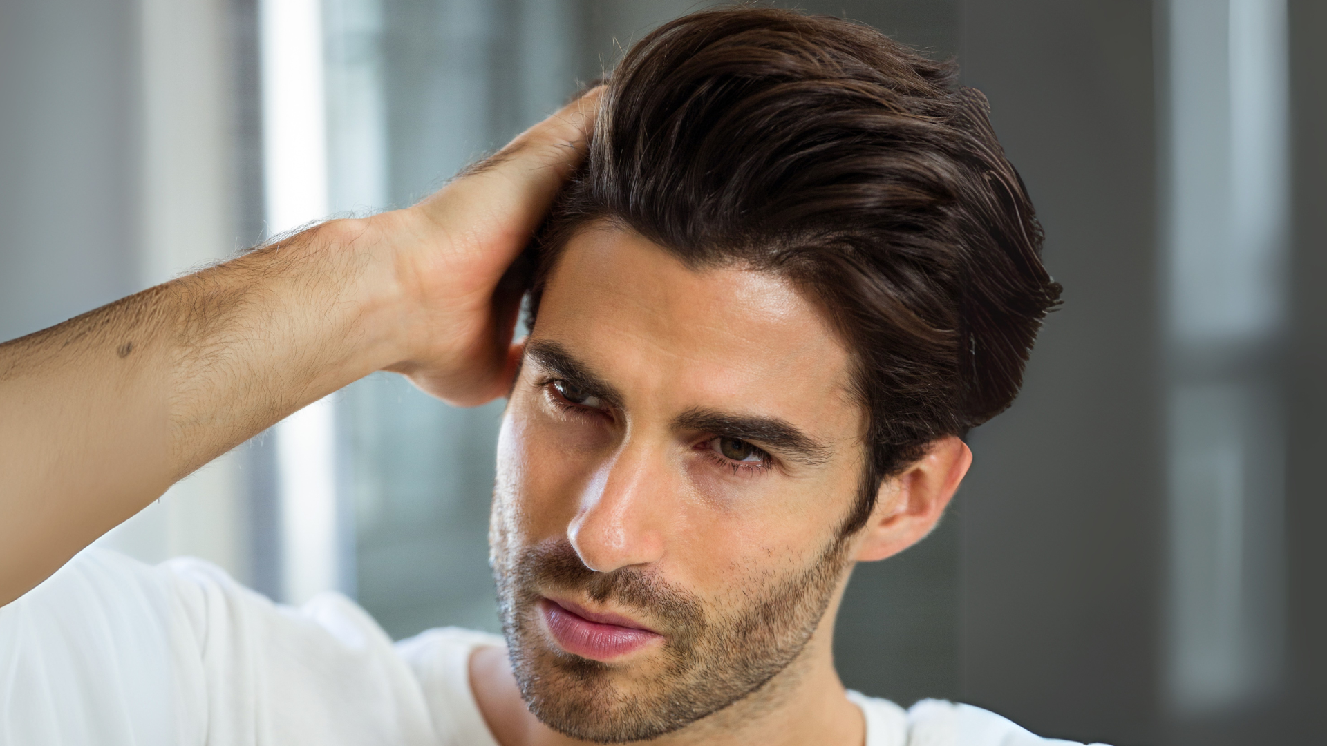 A man is looking at his hair in the mirror.