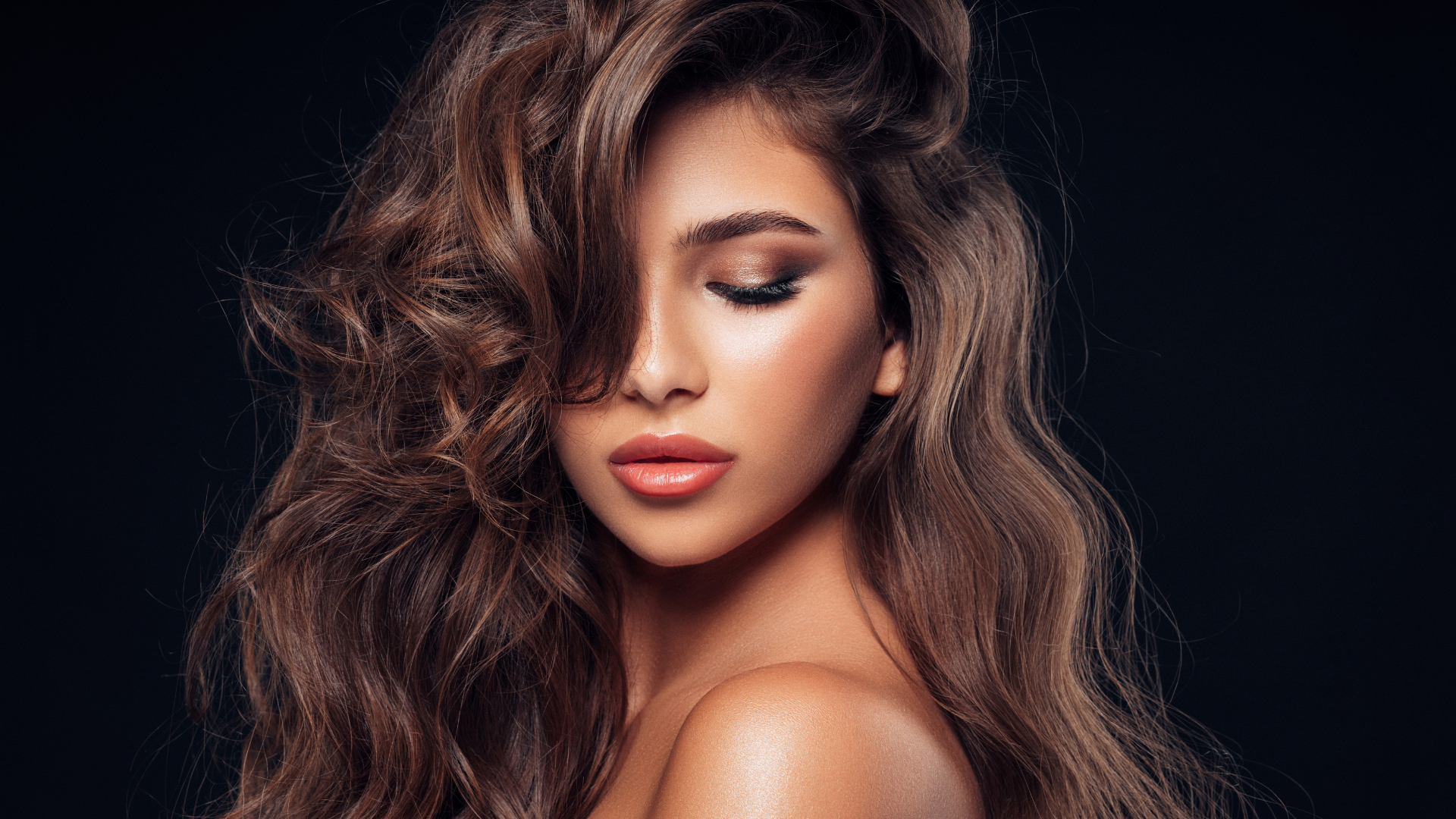 A woman with long brown hair is covering her face with her hair.