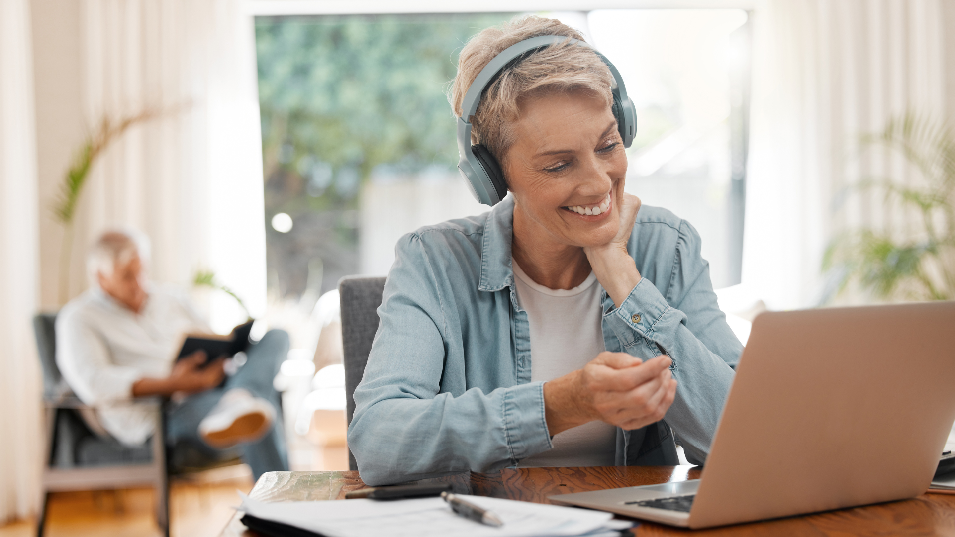 A woman wearing headphones is sitting at a desk using a laptop computer.