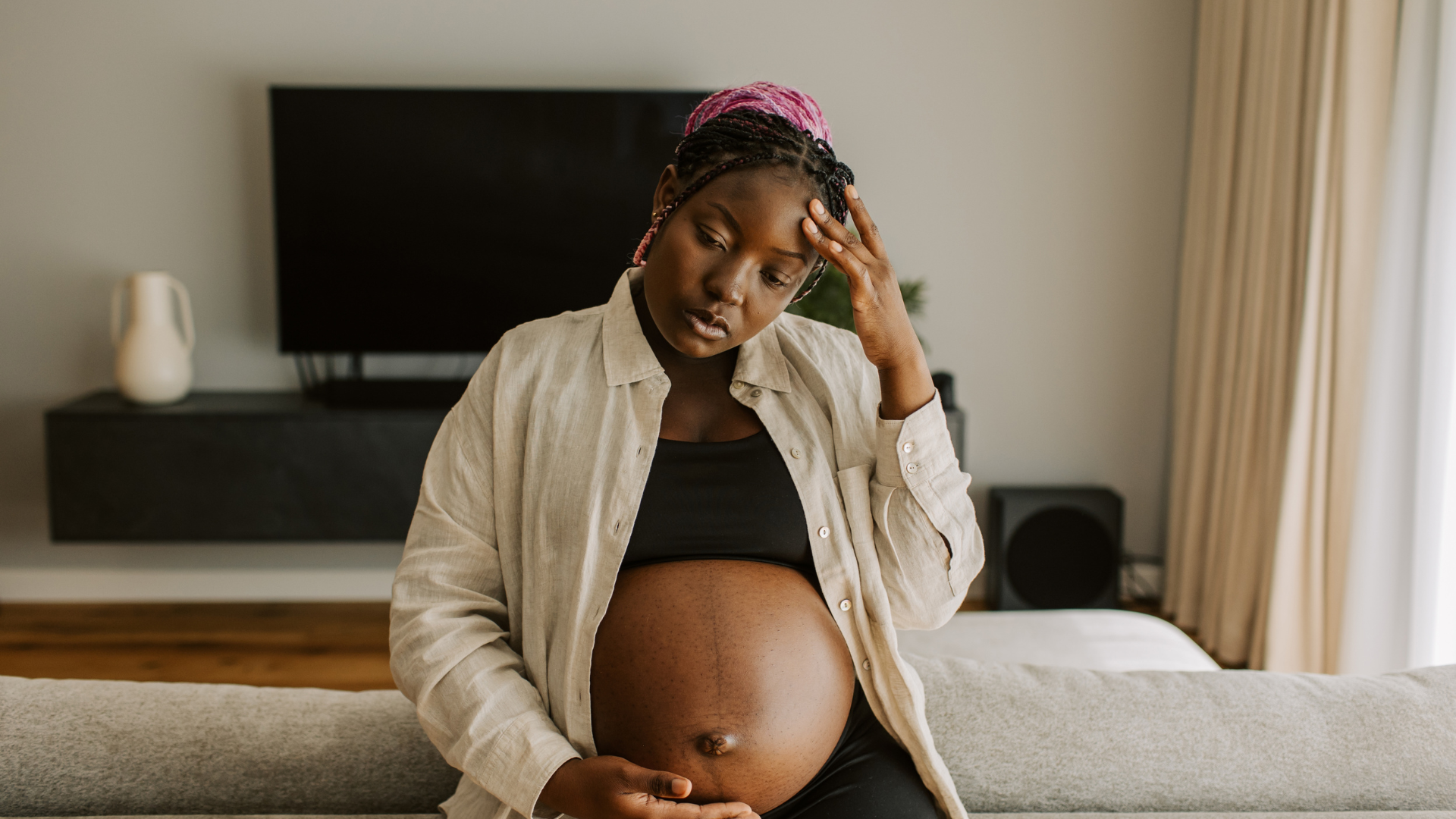A pregnant woman is sitting on a couch holding her belly.