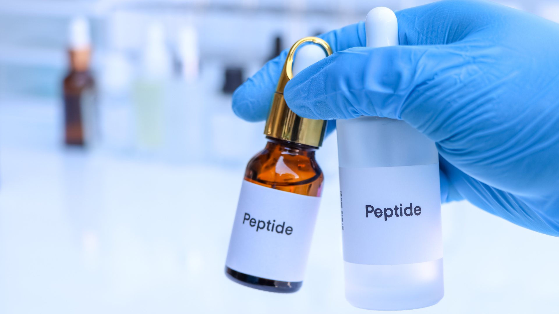 A person in a blue glove is holding two bottles of peptides.