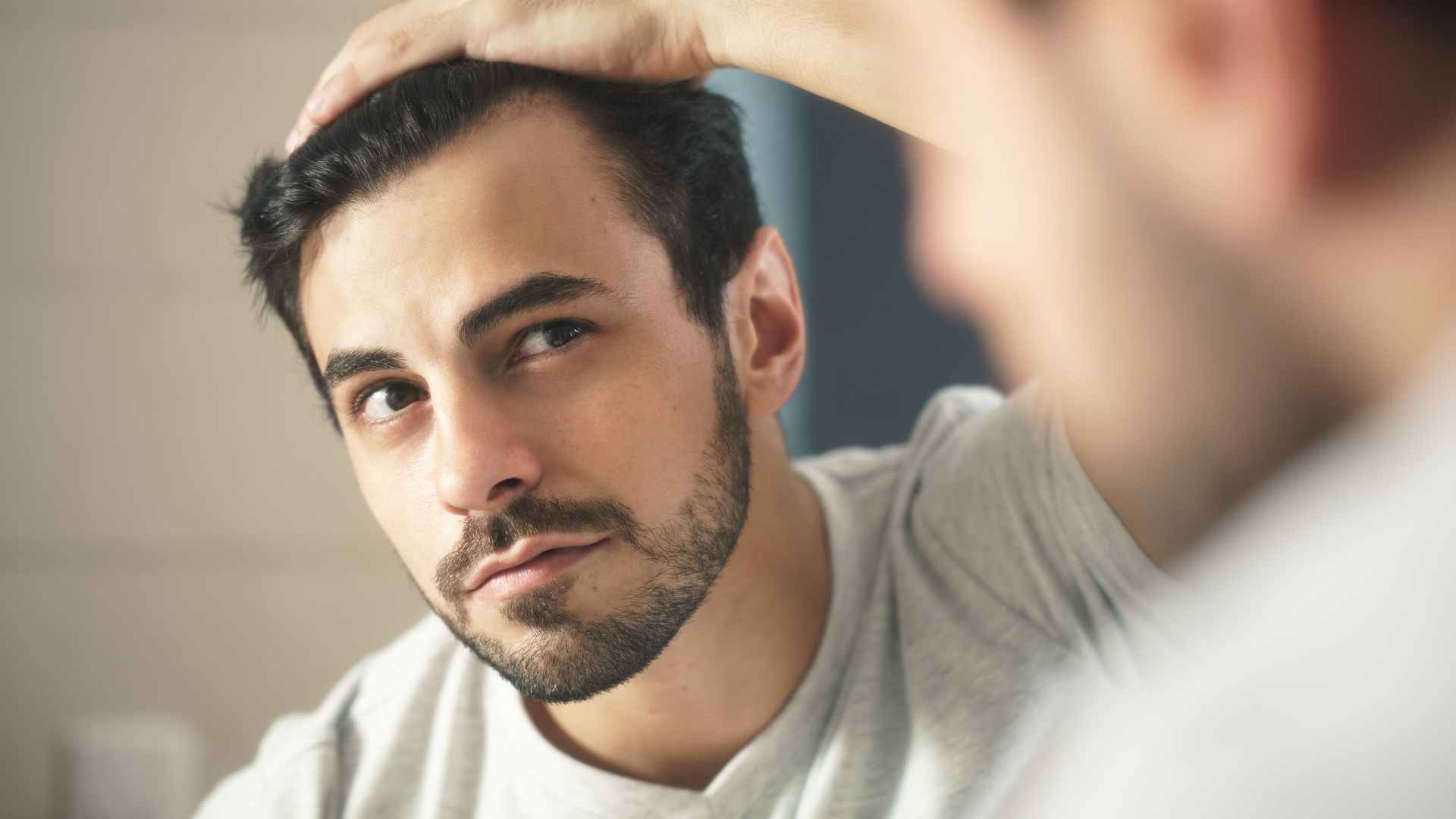 A man is looking at his hair in the mirror.