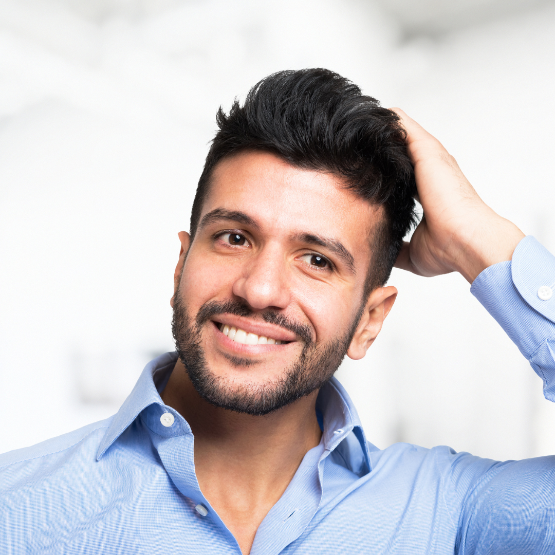 A man with a beard is smiling and touching his hair