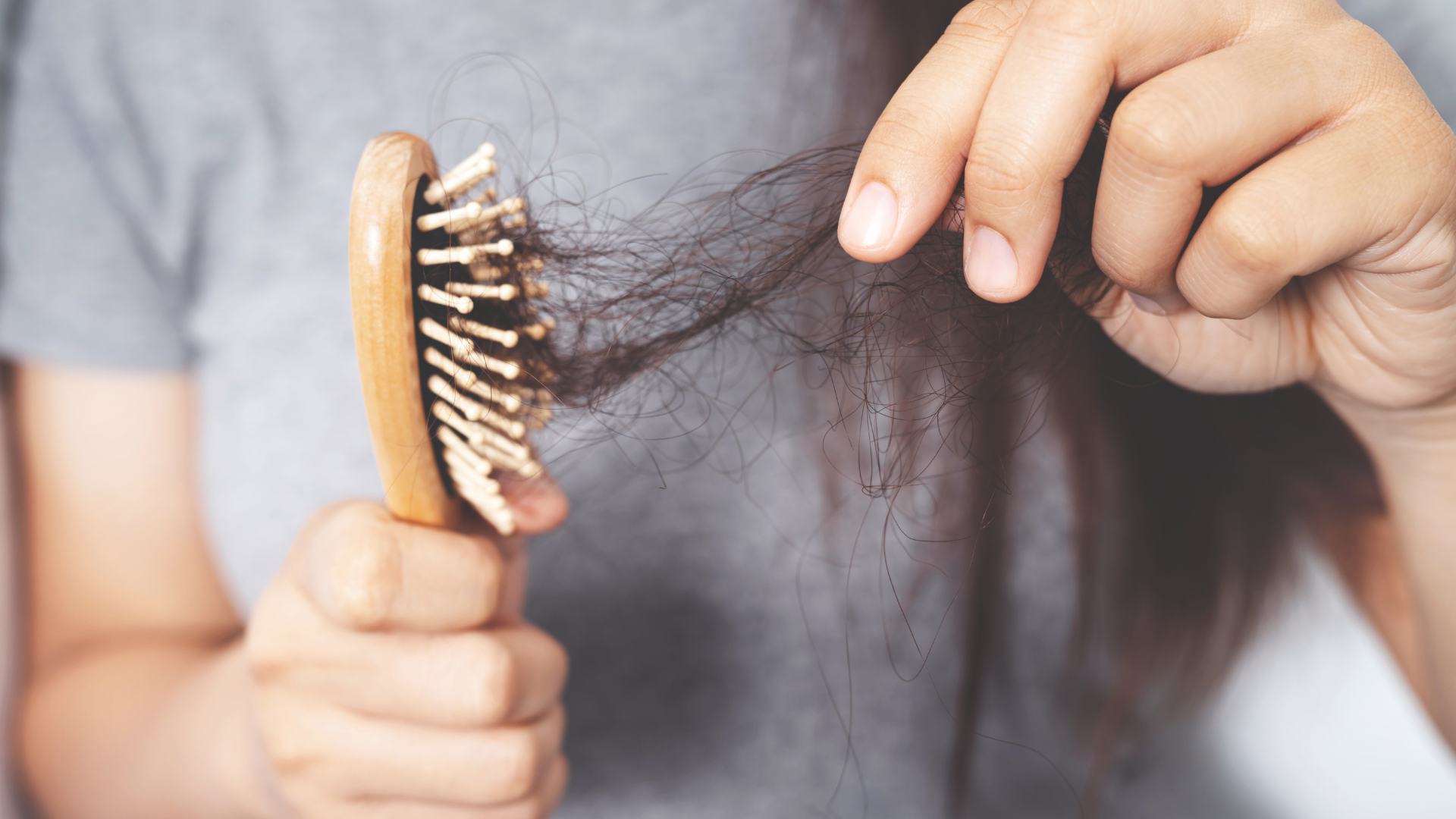 A woman is brushing her hair with a wooden brush.