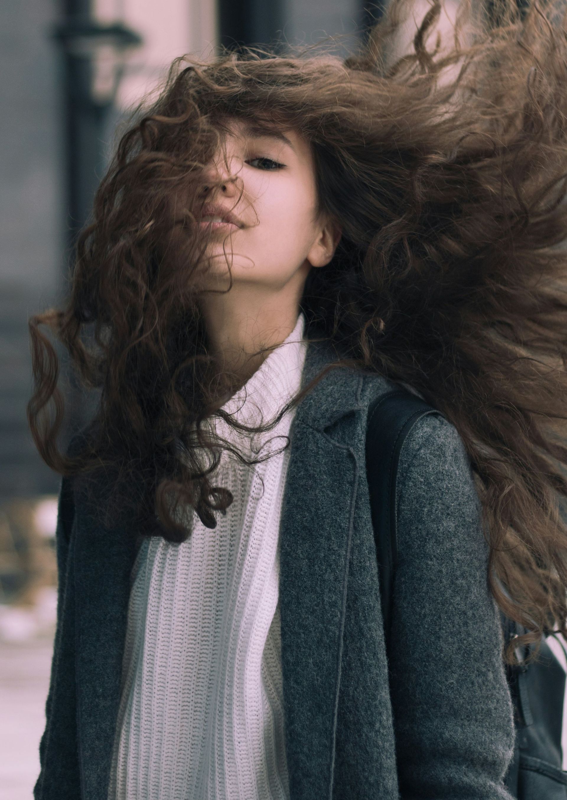 A woman with long curly hair is blowing her hair in the wind.