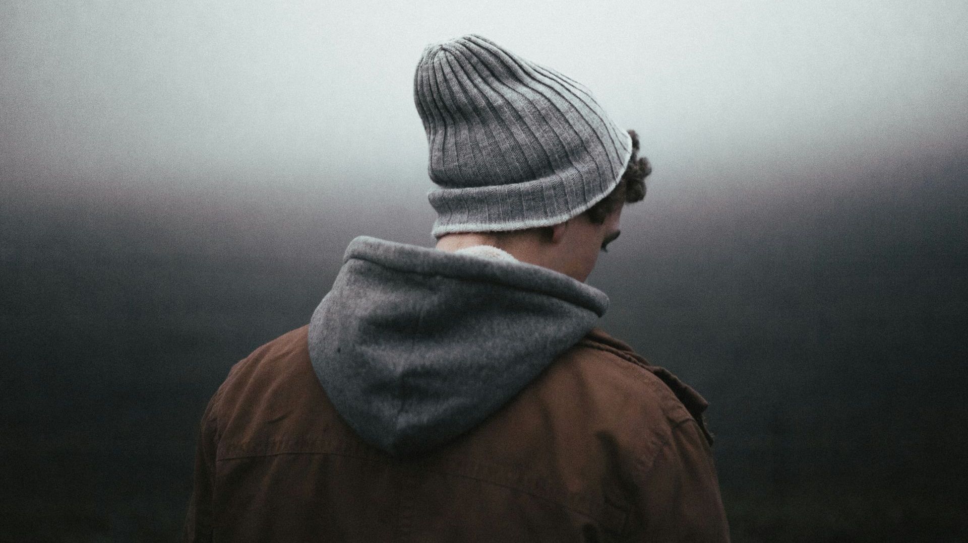 A man wearing a beanie and a hoodie is standing in the fog.