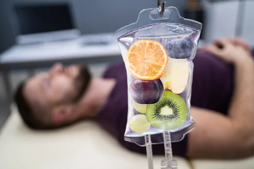 A man is laying on a bed with a bag of fruit in his veins.