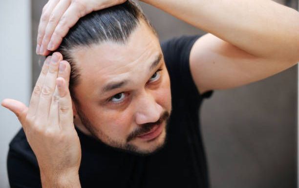 A man with a beard is looking at his hair in the mirror.