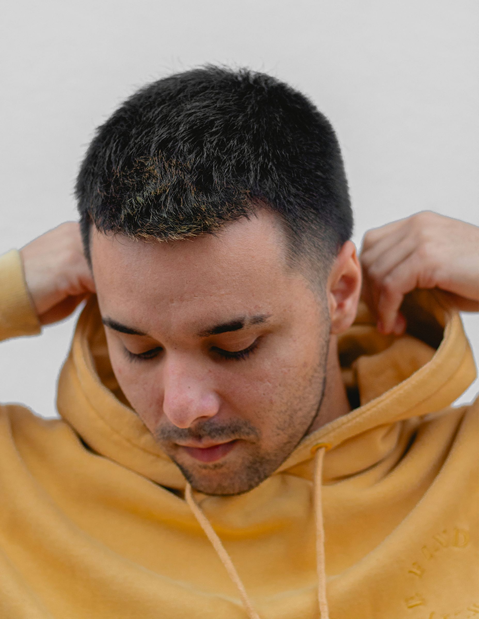 A man wearing a yellow hoodie is adjusting his hood.