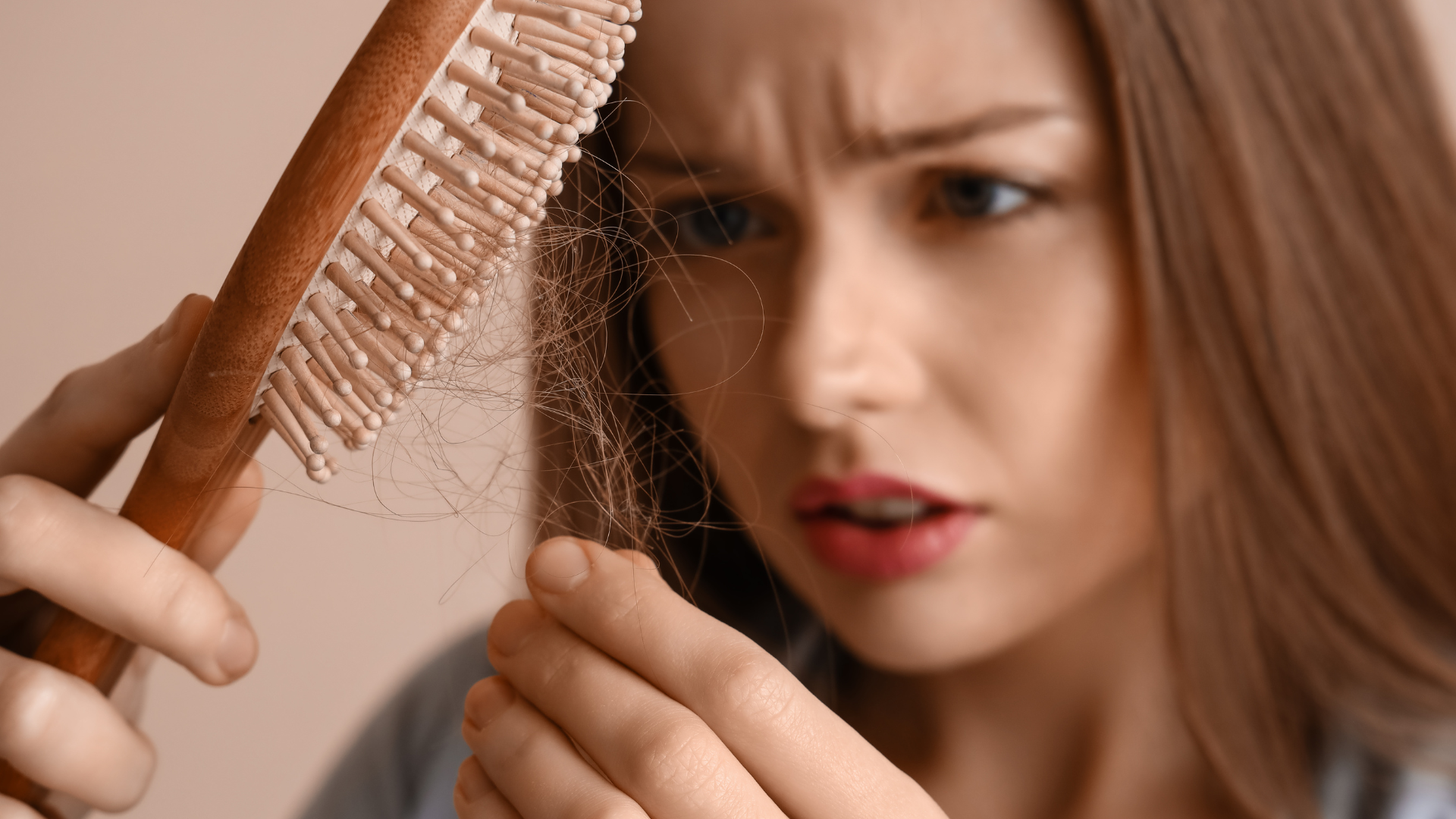 A woman is holding a brush and looking at her hair.