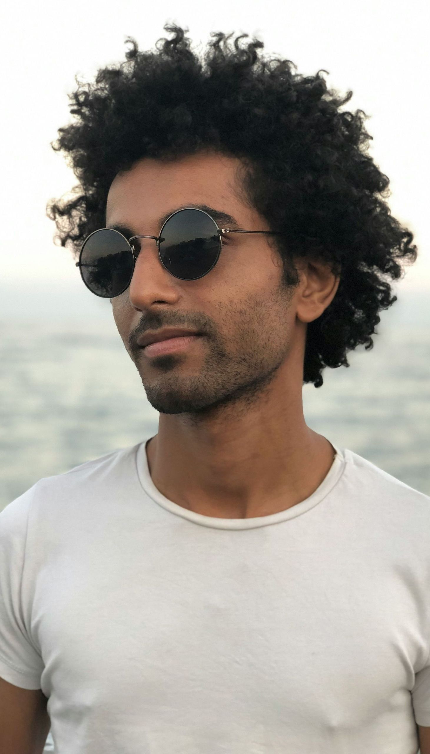 A man with curly hair wearing sunglasses and a white shirt