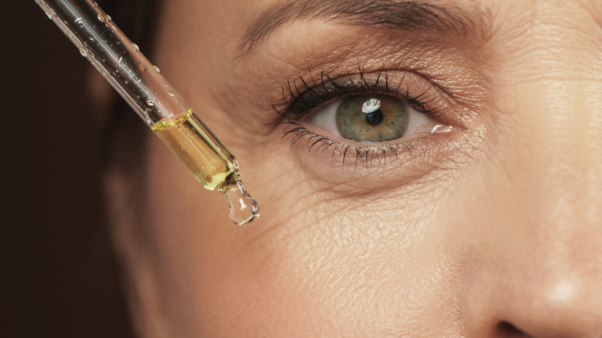 A woman is applying a drop of serum to her eye.
