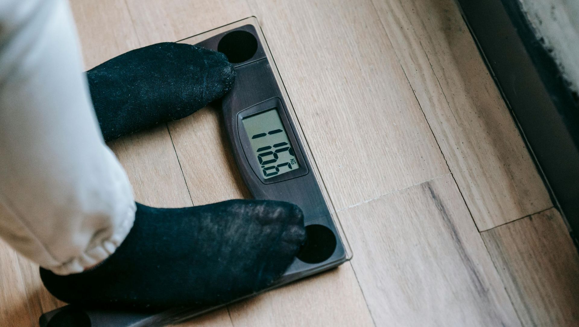 Feet in black socks stand on a digital scale; the display shows 116.8. The scale is on a light wood floor.