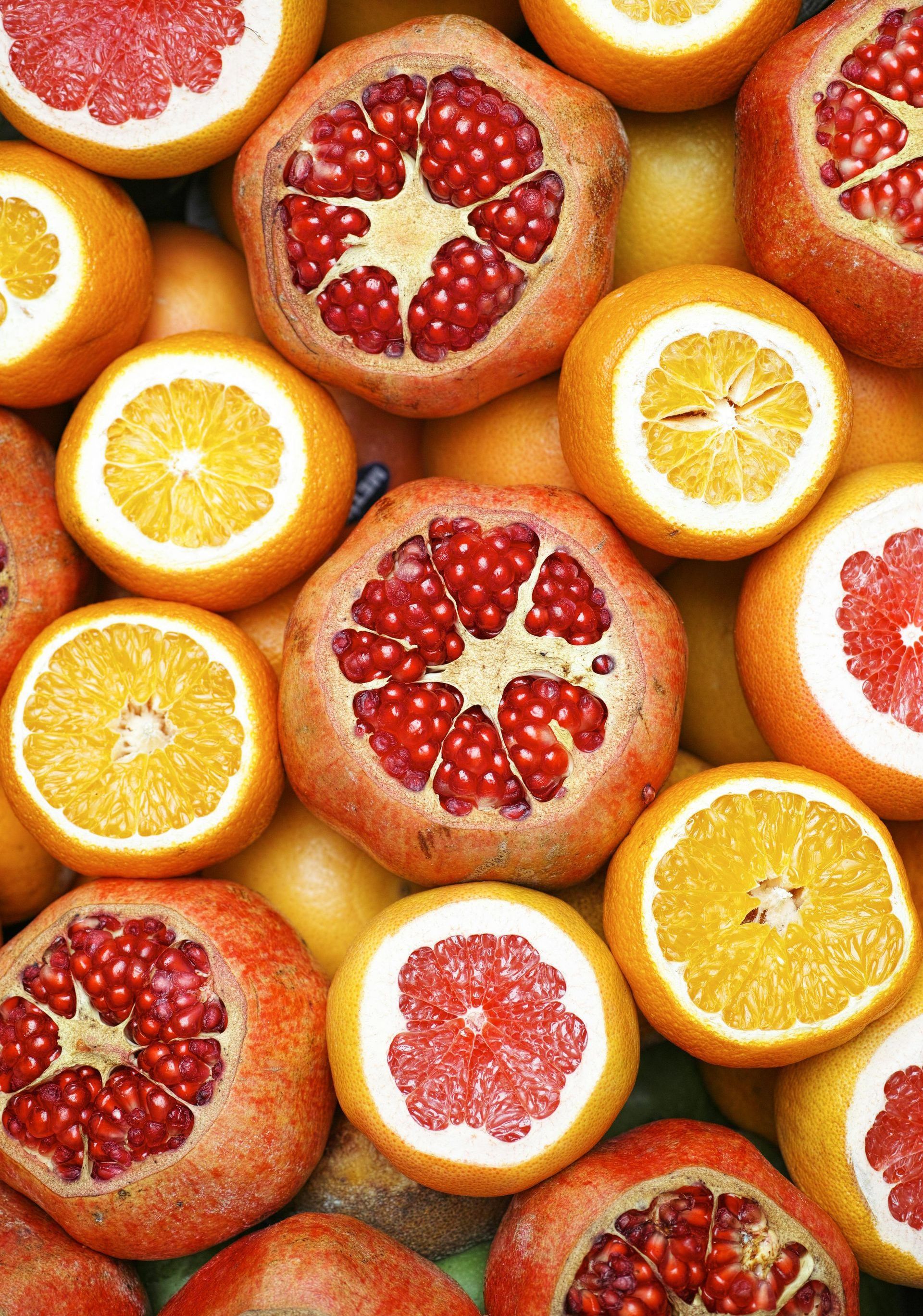 A pile of oranges and pomegranates cut in half