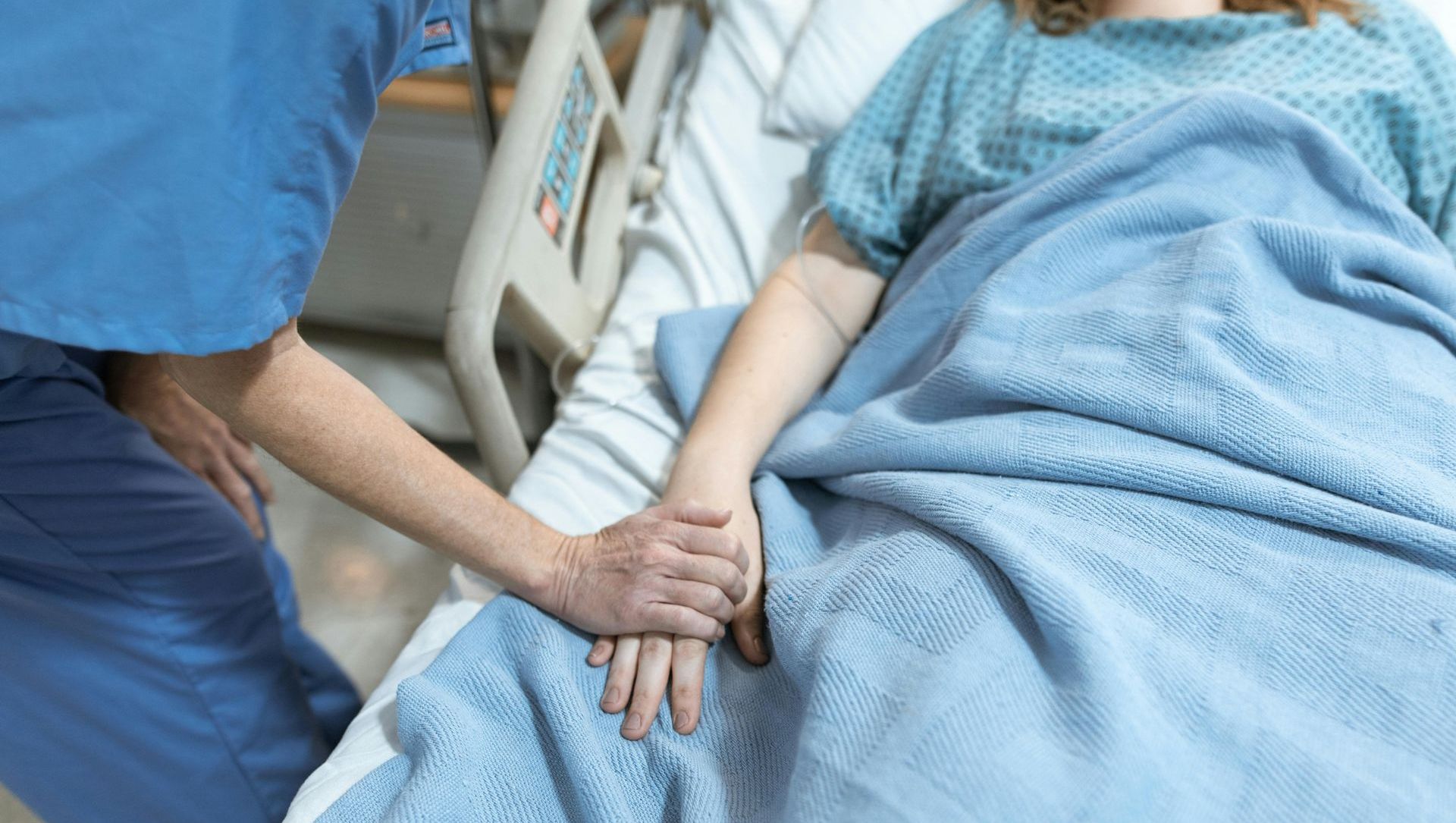 A nurse is holding the hand of a patient in a hospital bed.
