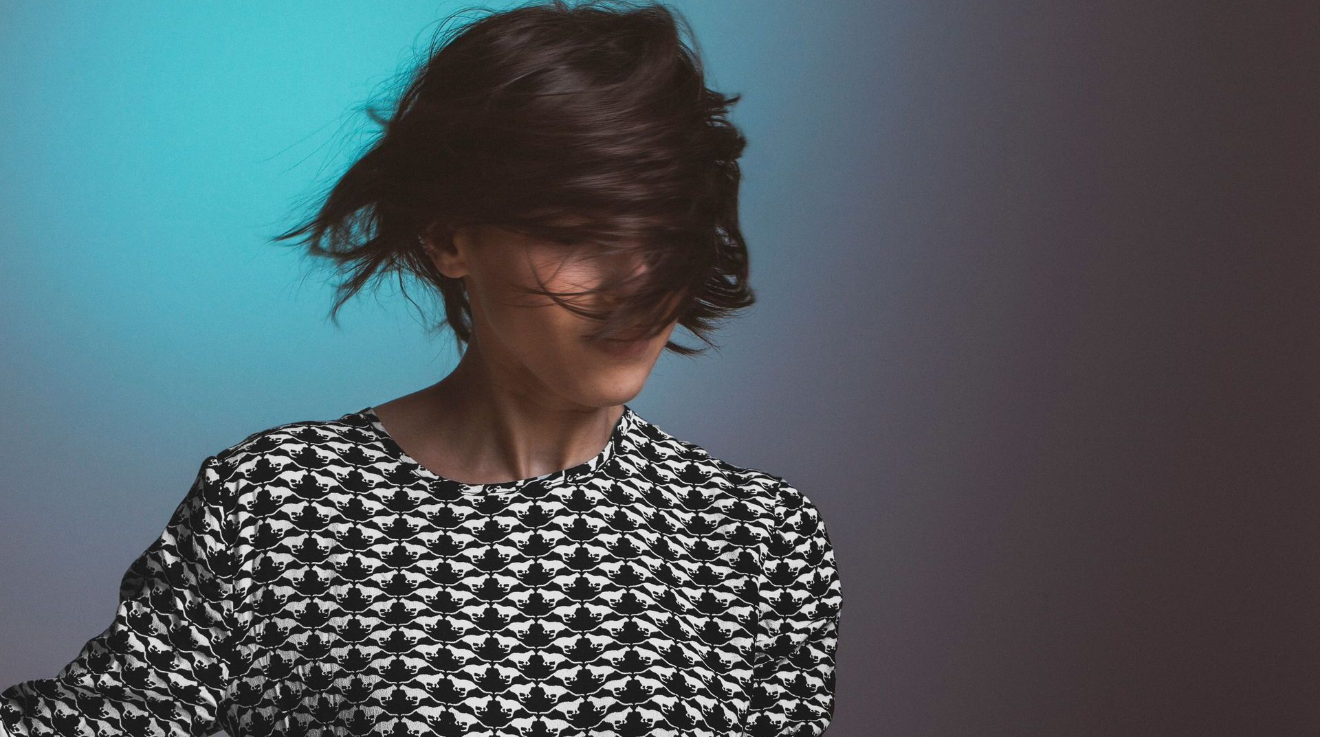 A woman in a black and white dress is dancing with her hair blowing in the wind.