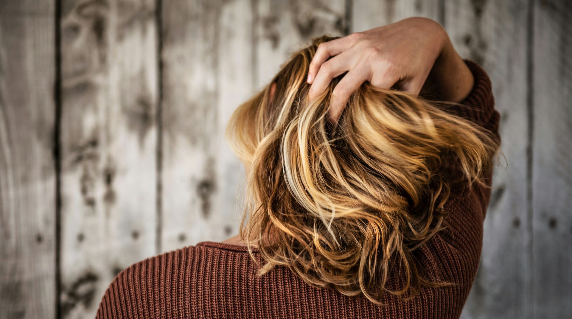 A woman is scratching her head in front of a wooden wall.