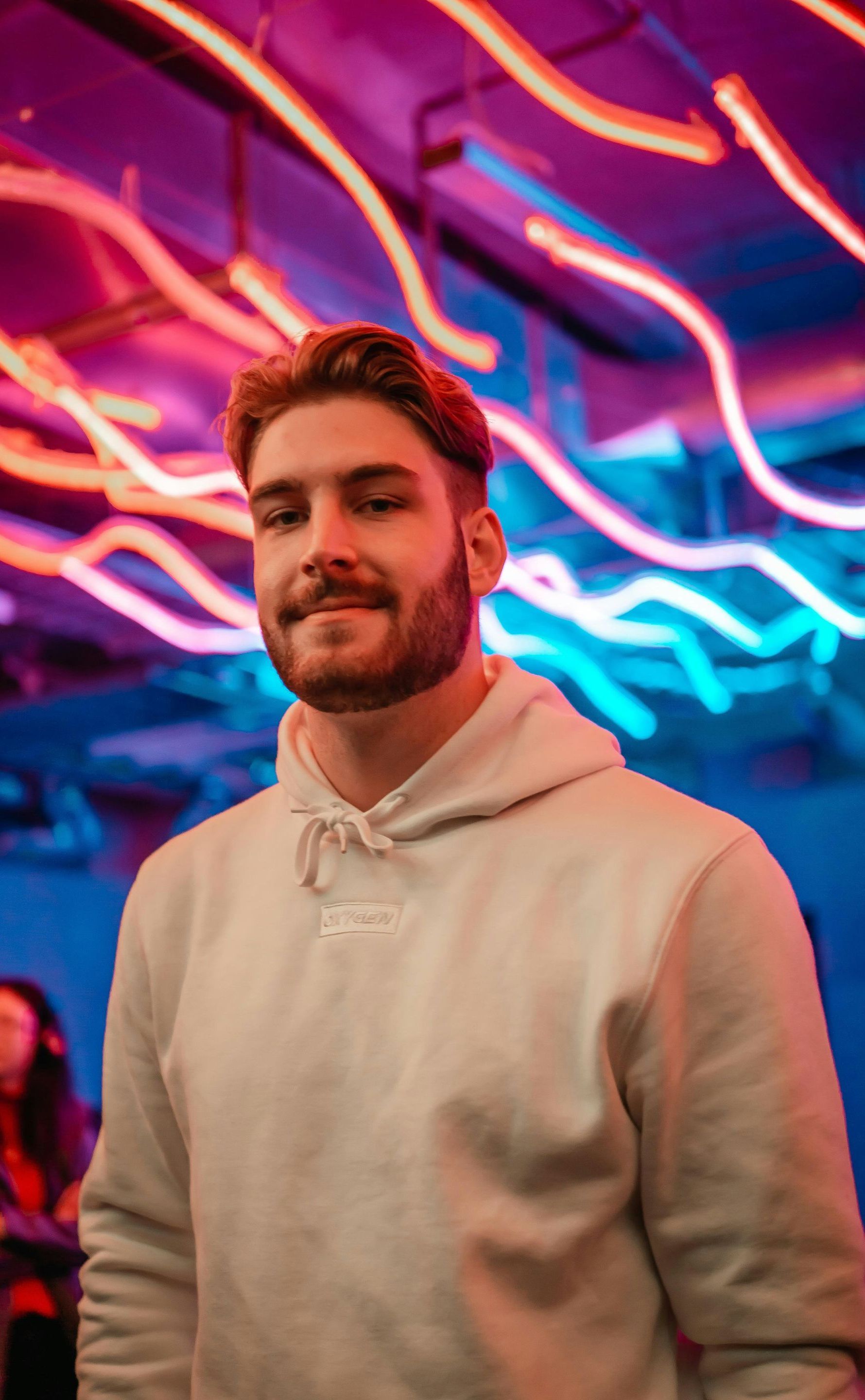 A man with a beard is standing in front of a neon sign.