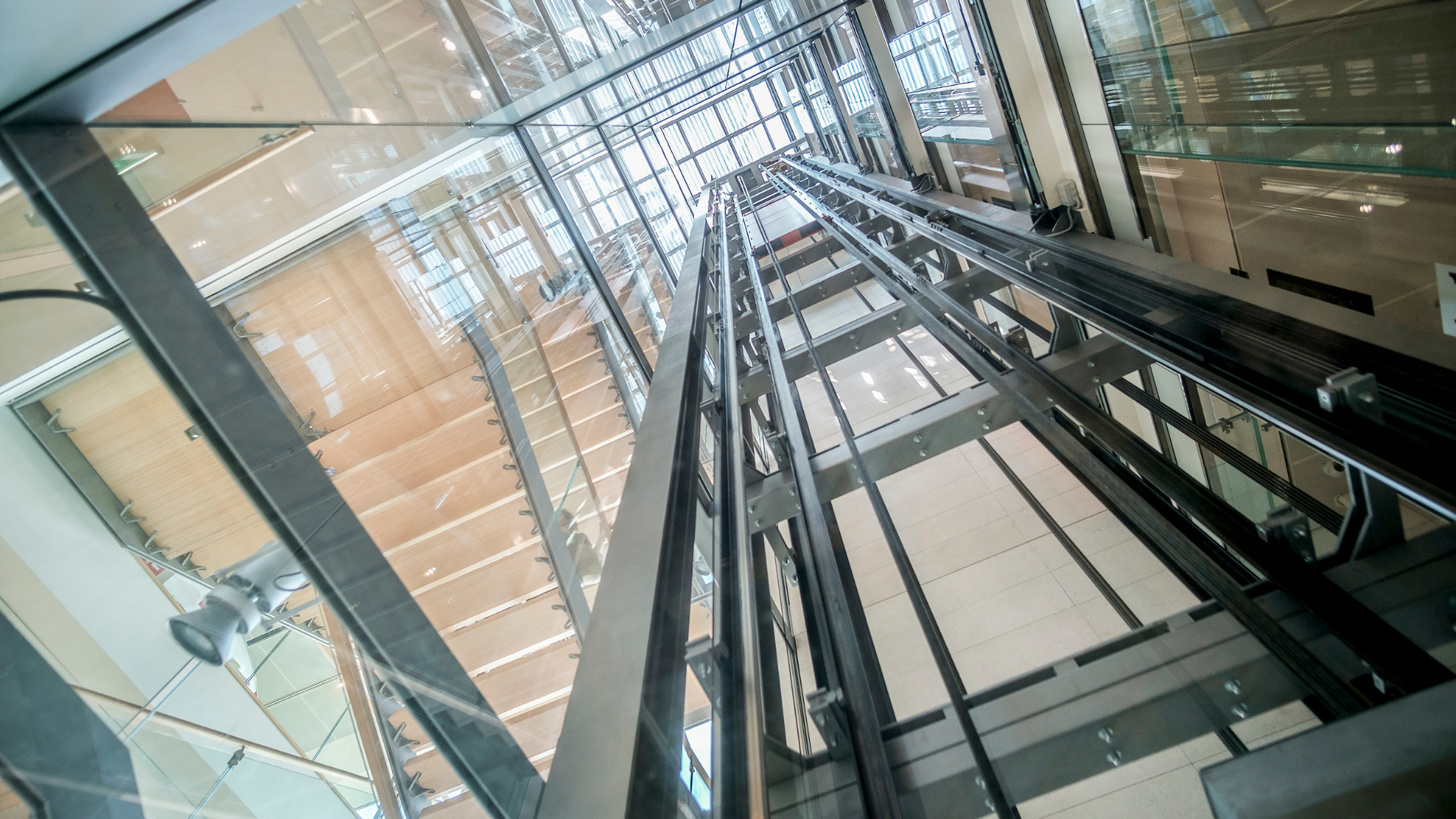 Looking up at a modern glass elevator shaft with cables and metal framework.