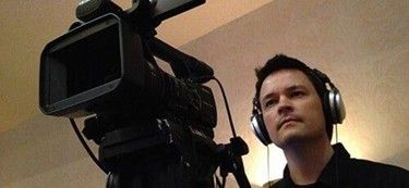 A man operating a professional video camera while wearing headphones during filming. A man operating a professional video camera while wearing headphones during filming.