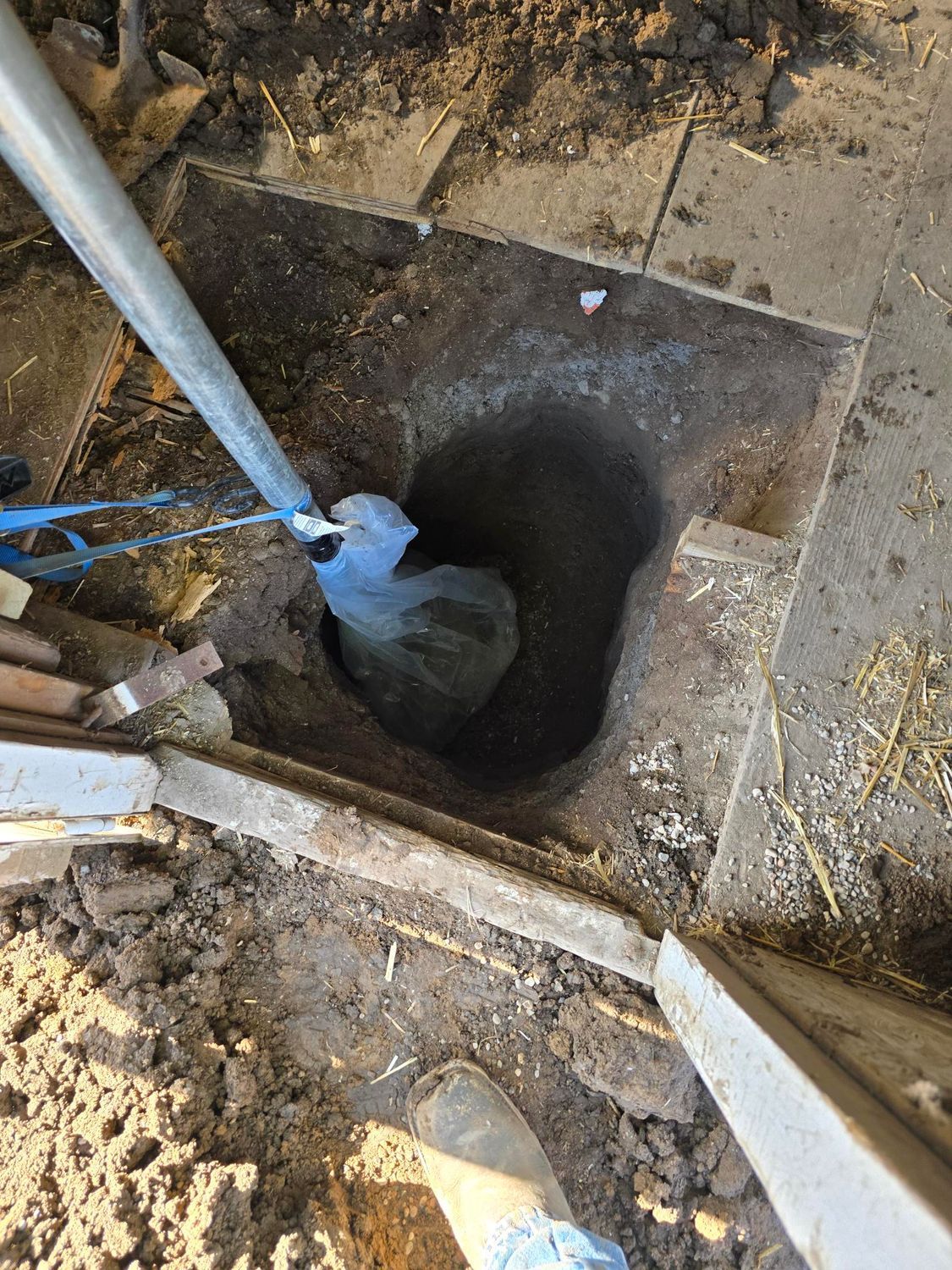 Hole dug in the ground, with a pole, shovel, and debris nearby.