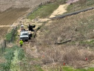 Workers near a white truck on a grassy hillside next to a fence and a railway.
