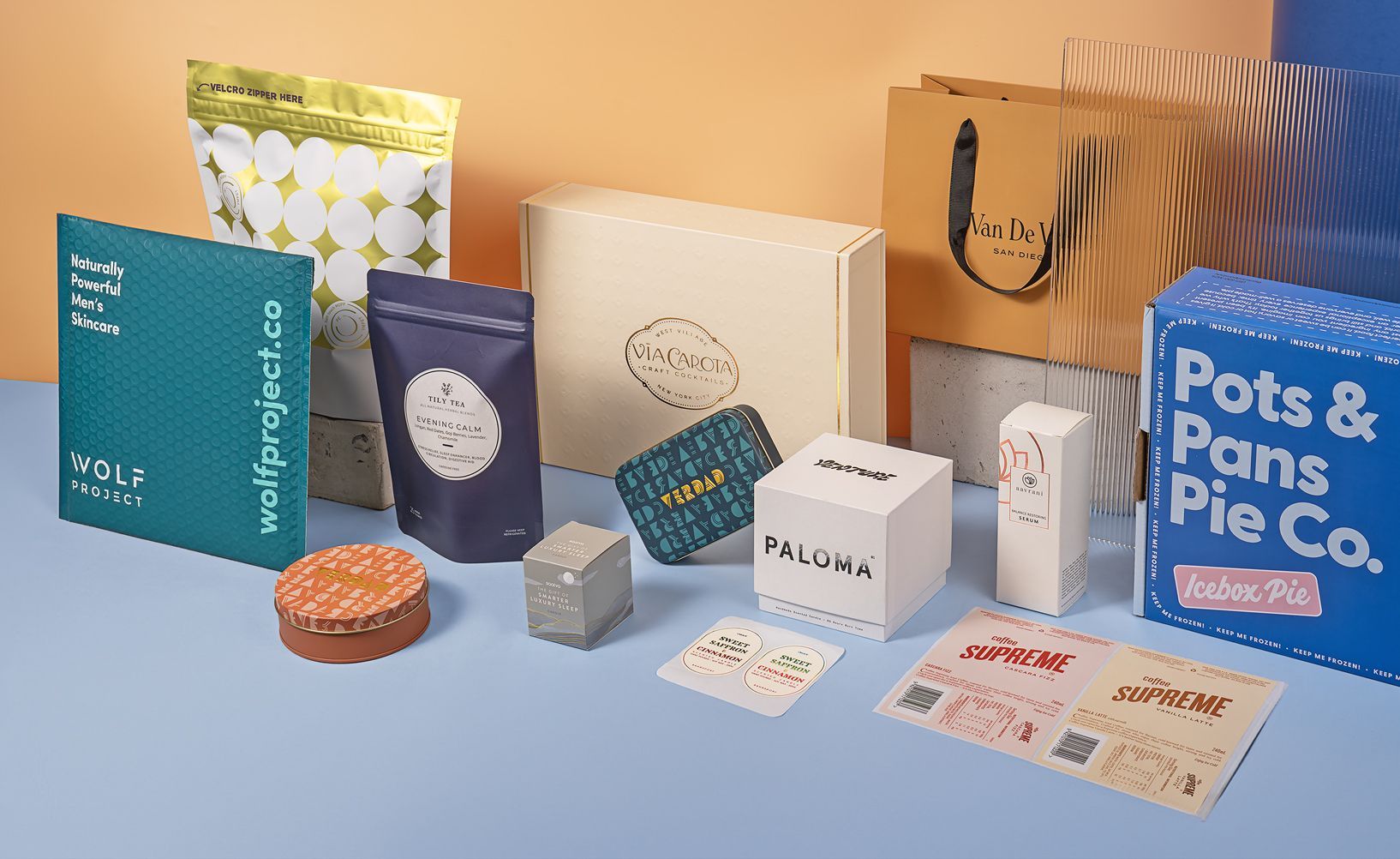 Assorted product packaging including bags, boxes, and labels; in beige, blue, and gold tones.