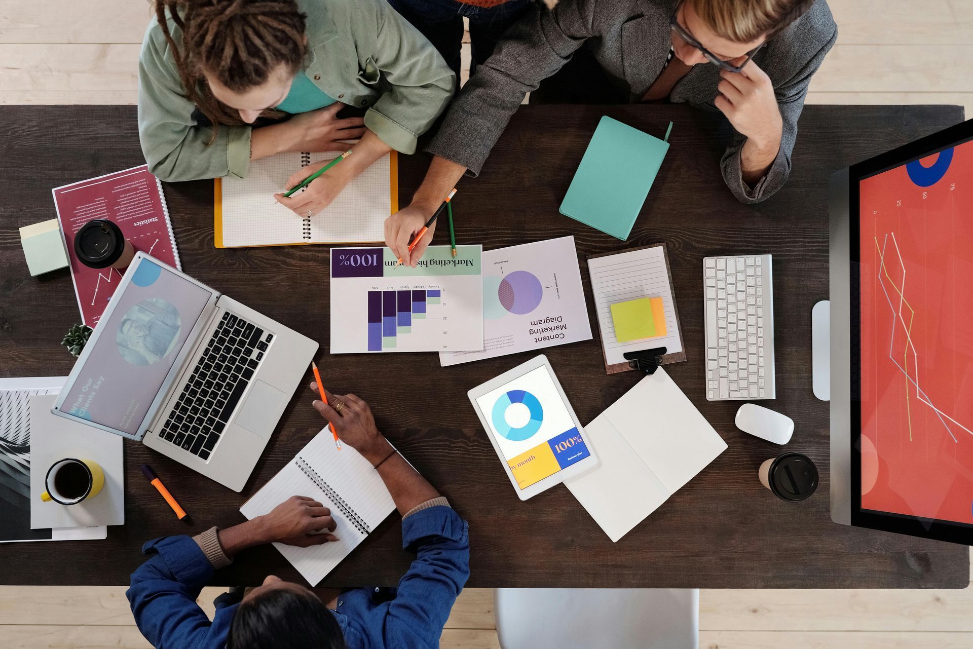 People collaborating around a table with laptops, charts, and notebooks.