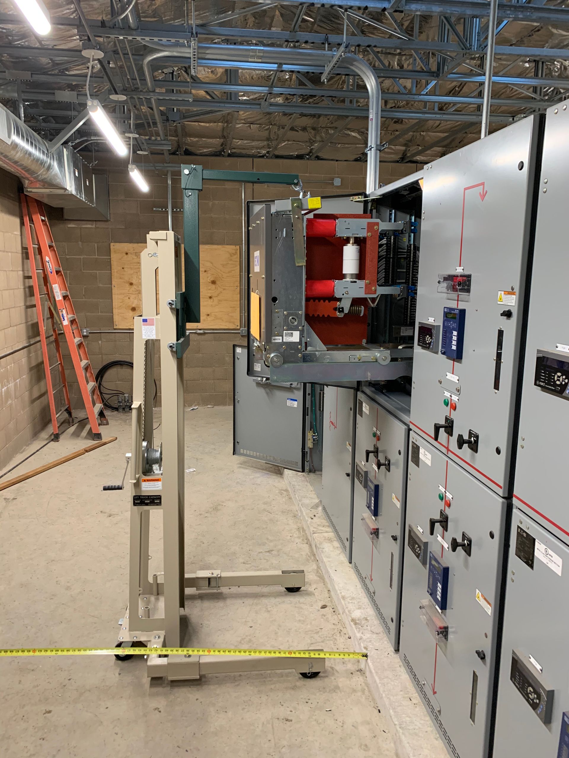 Electrical equipment in a construction site, with a gray panel, red circuit breakers, and a lift device.