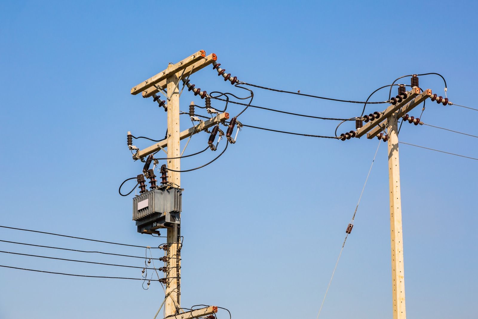 Utility poles with transformers and power lines against a clear blue sky.