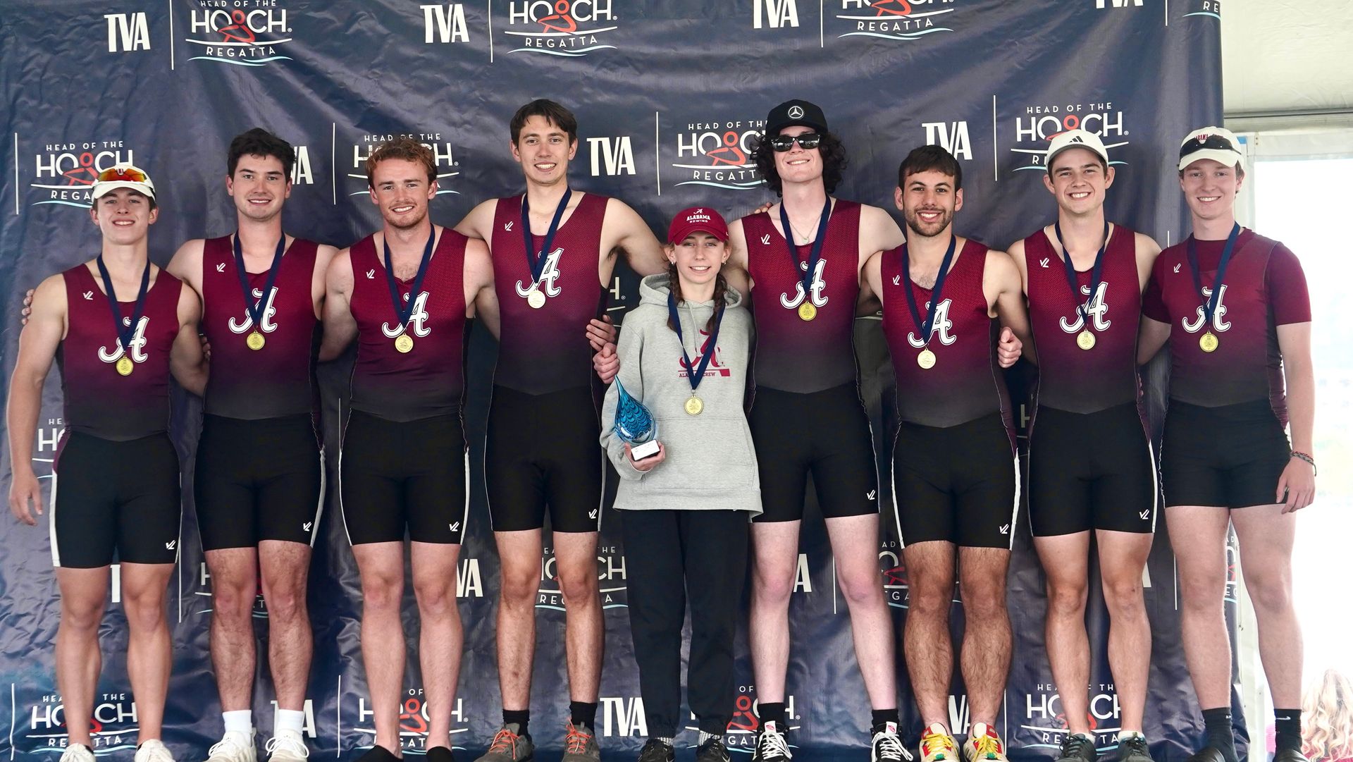A group of people wearing medals stand on a podium. They are posing for a picture, smiling, with a banner behind them.