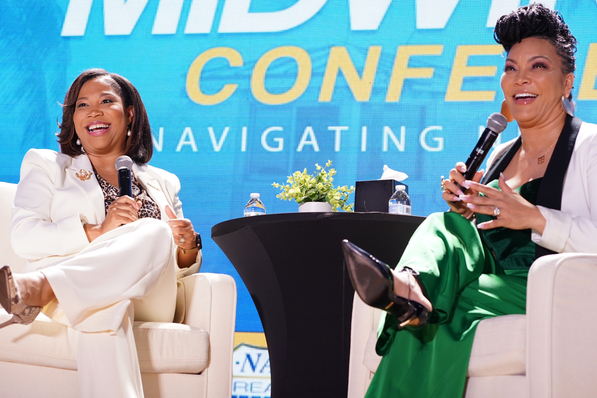 Courtney and a colleague speaking on stage at a conference, seated in white chairs with microphones and a blue backdrop.